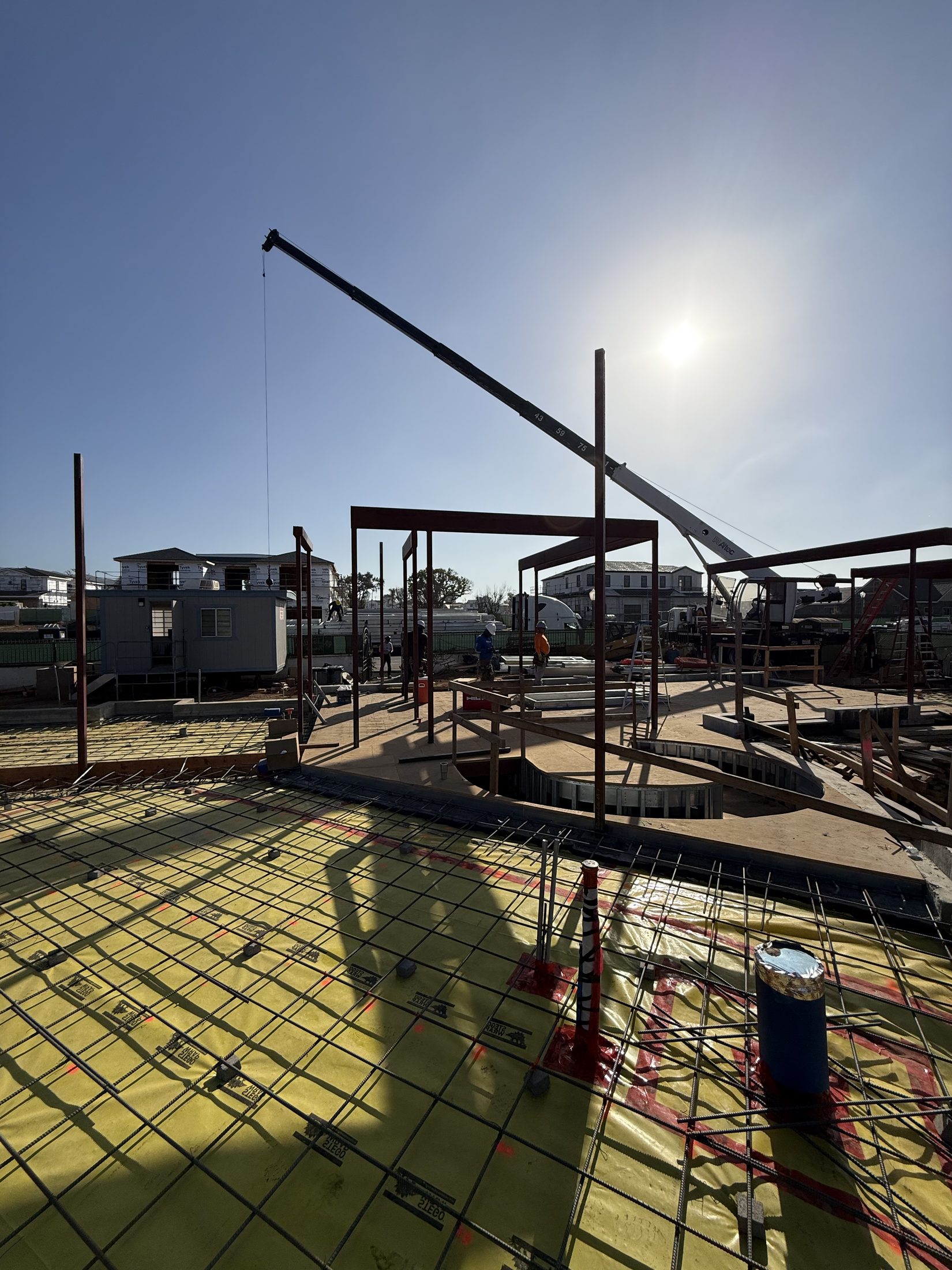 Structural steel columns rising over the ground-floor slab with the crane beyond at 777 Ocampo